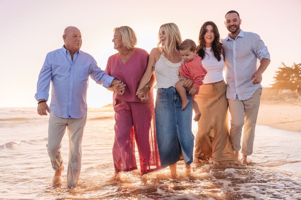 Happy multi-generational family walking together on a beach at golden sunset, smiling and holding hands.