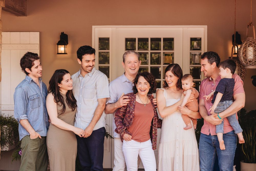 Multi-generational Asian family smiling together outside a home entrance during a casual portrait session.