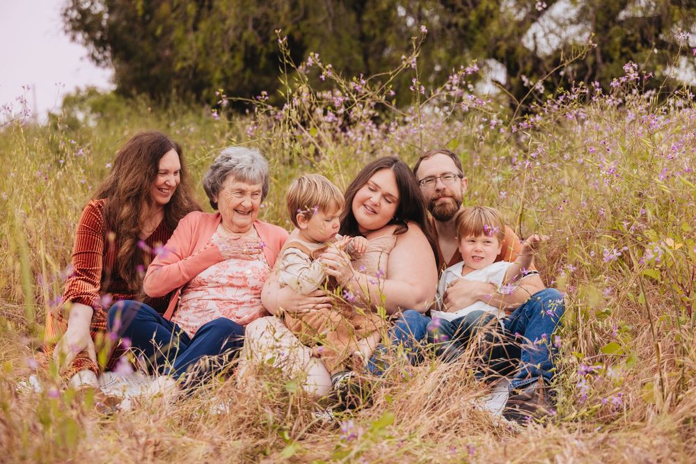 Multi-generational family sitting together in a wildflower meadow, smiling and embracing outdoors.