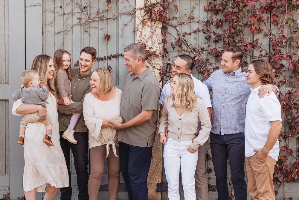A large multigenerational family smiling and laughing together outdoors against a rustic wall with autumn red ivy.