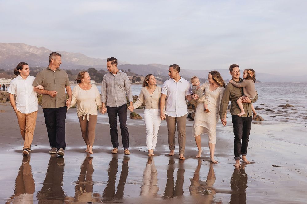 Large family walking together on a sandy beach at sunset with mountains in the background.