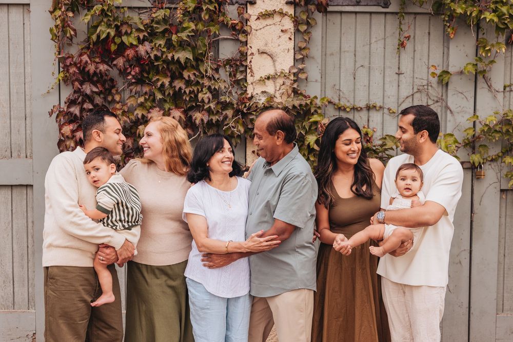 Multigenerational family smiling together outdoors in front of a rustic wall with autumn ivy.