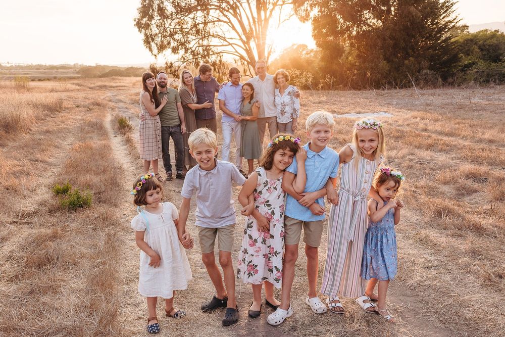 Large family group portrait at golden hour in a dry field, children in front smiling, adults gathered behind them.