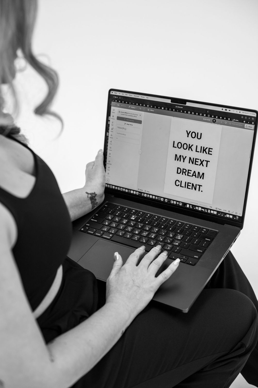 Woman holding laptop displaying 'You Look Like My Next Dream Client' text in black and white photo.