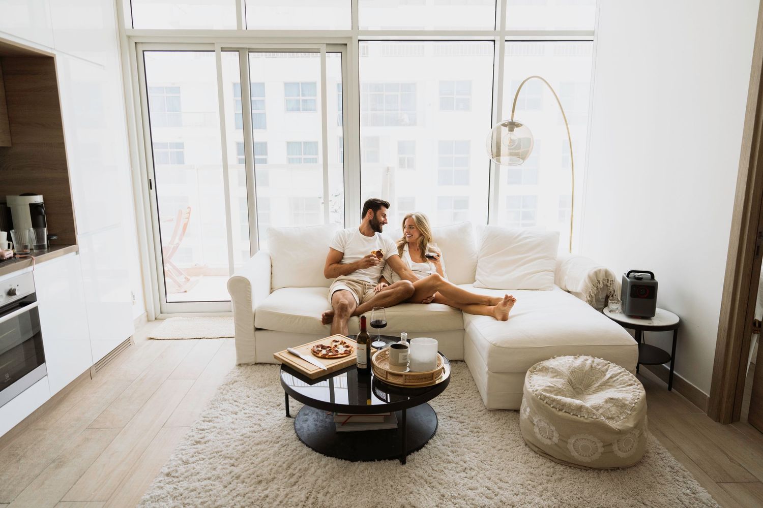 Intimate couple photoshoot in a luxury, bright living room featuring a couple laughing on a large white sofa with natural light.