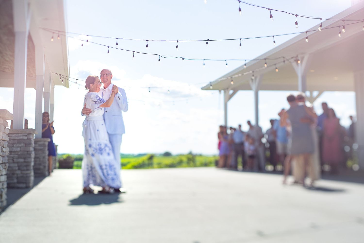 A couple shares their first dance at an outdoor wedding pavilion with guests watching in the background.  Iowa City wedding photographer.