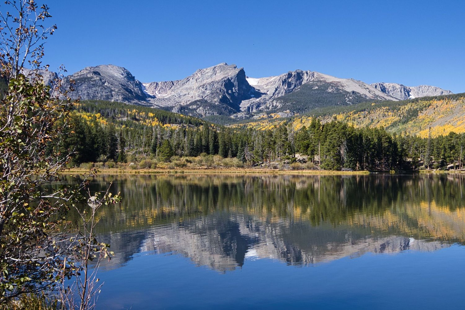 Hallets Peak and Flattop Mountain reflect on Sprague Lake. The Moraine is covered in golden aspen trees.