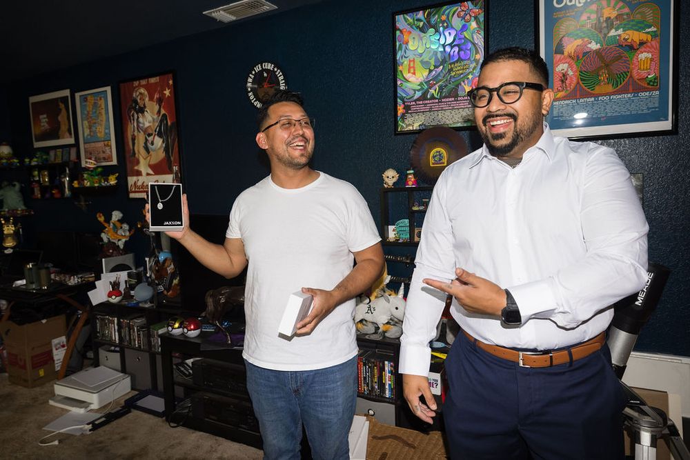 Two men laughing and holding devices in a colorful art-filled room.