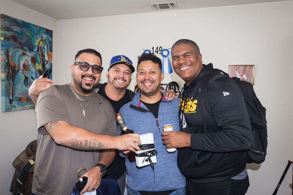 Four smiling men posing together indoors at a casual social gathering.