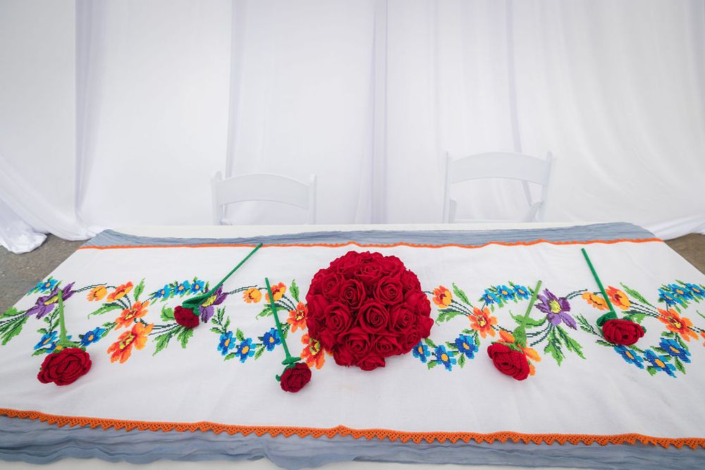 Elegant wedding table runner with colorful embroidered floral design and red rose bouquet centerpiece.