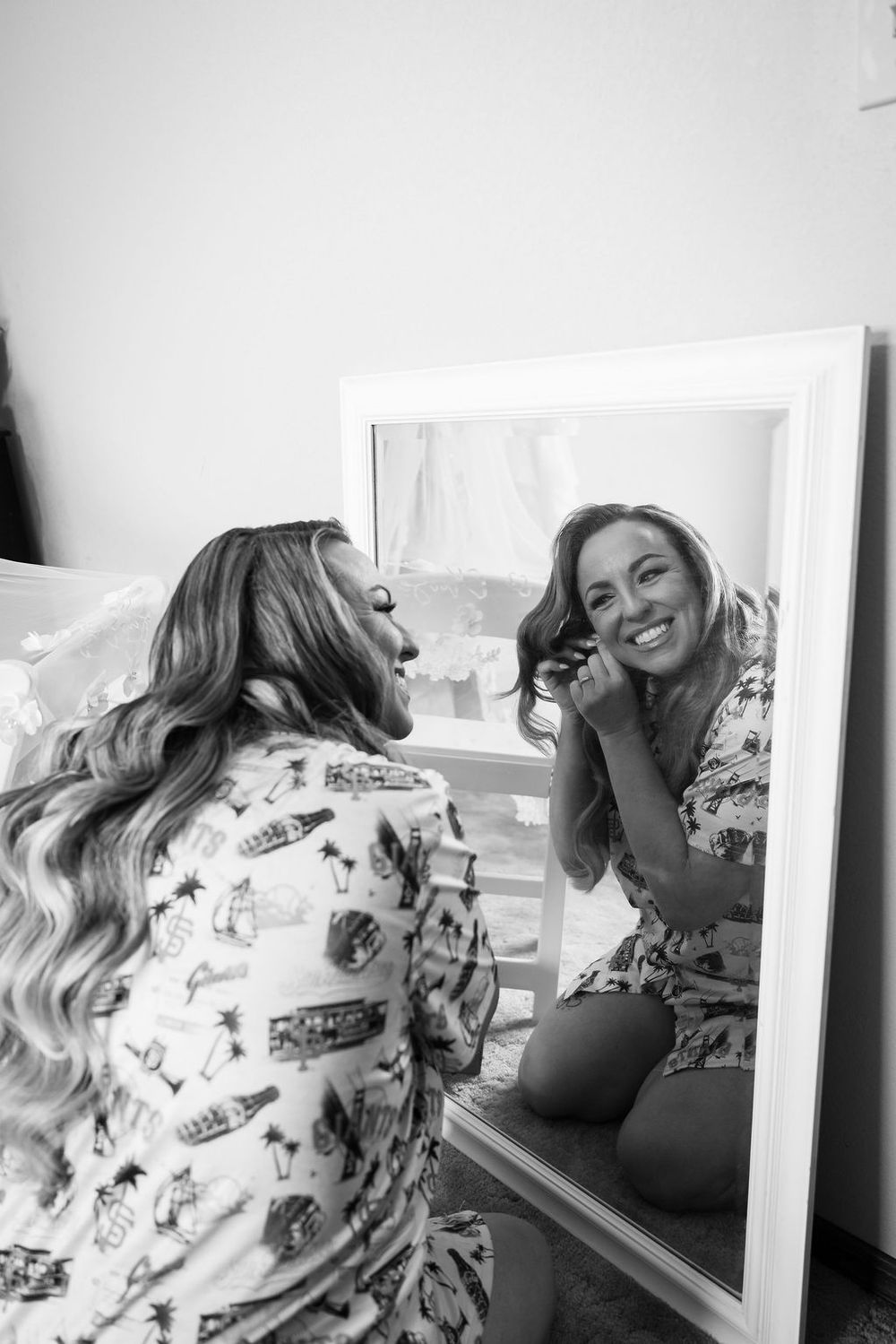 Black and white photo of a smiling woman doing her hair in front of a mirror while getting ready.