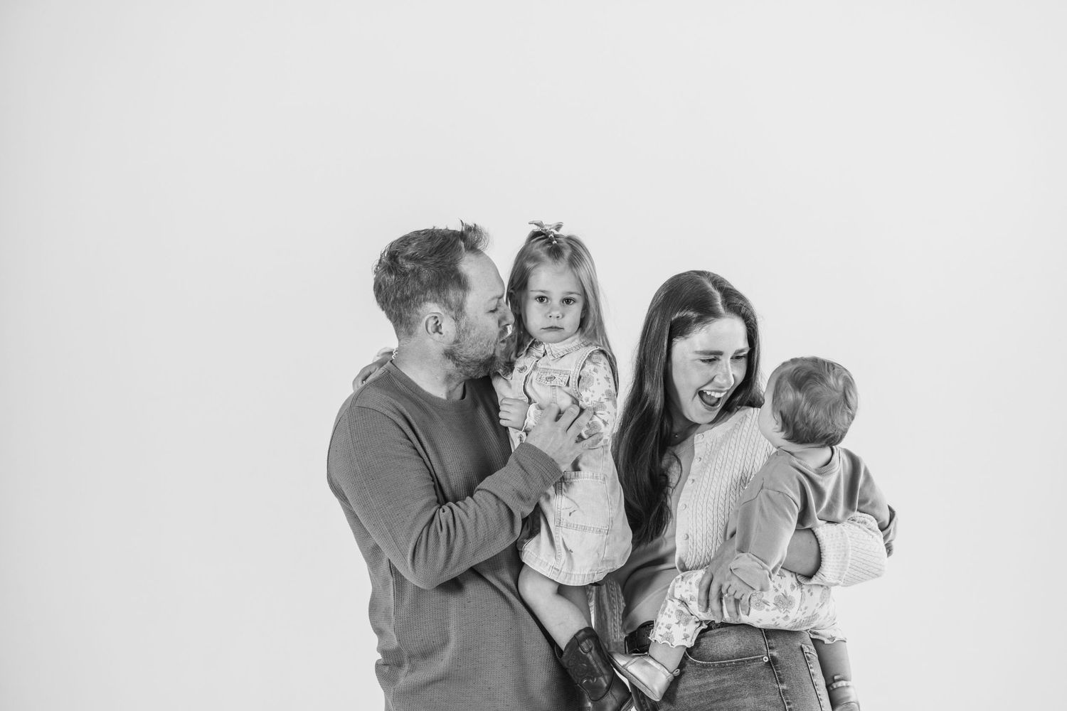 Black and white family portrait of parents holding two young children against a white background.