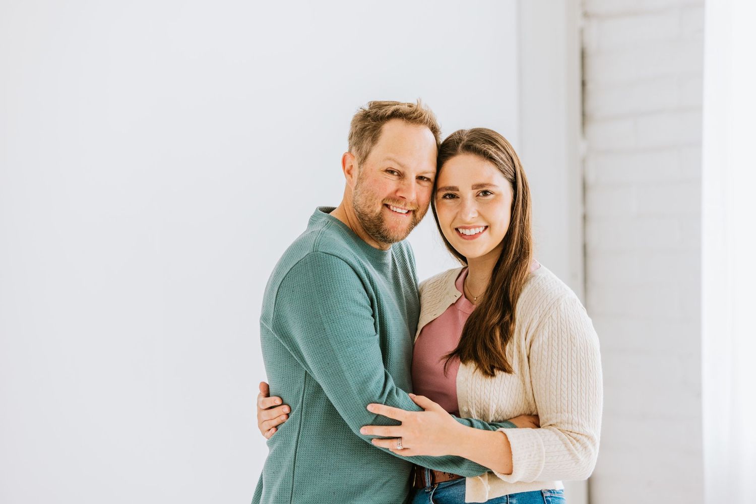 Happy couple embracing and smiling together against a bright white wall in a cozy studio portrait.