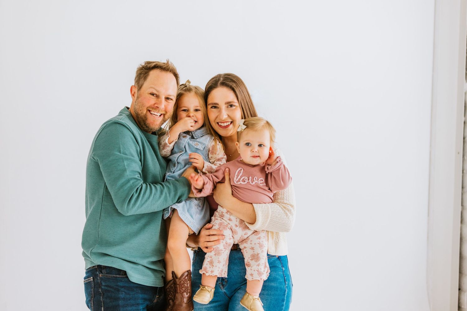 A smiling family of four posing together against a white background.