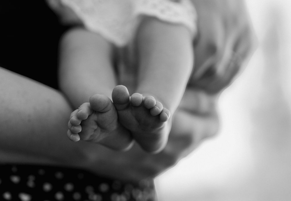 Black and white close-up photo of tiny newborn baby feet held gently in a parent's hands.