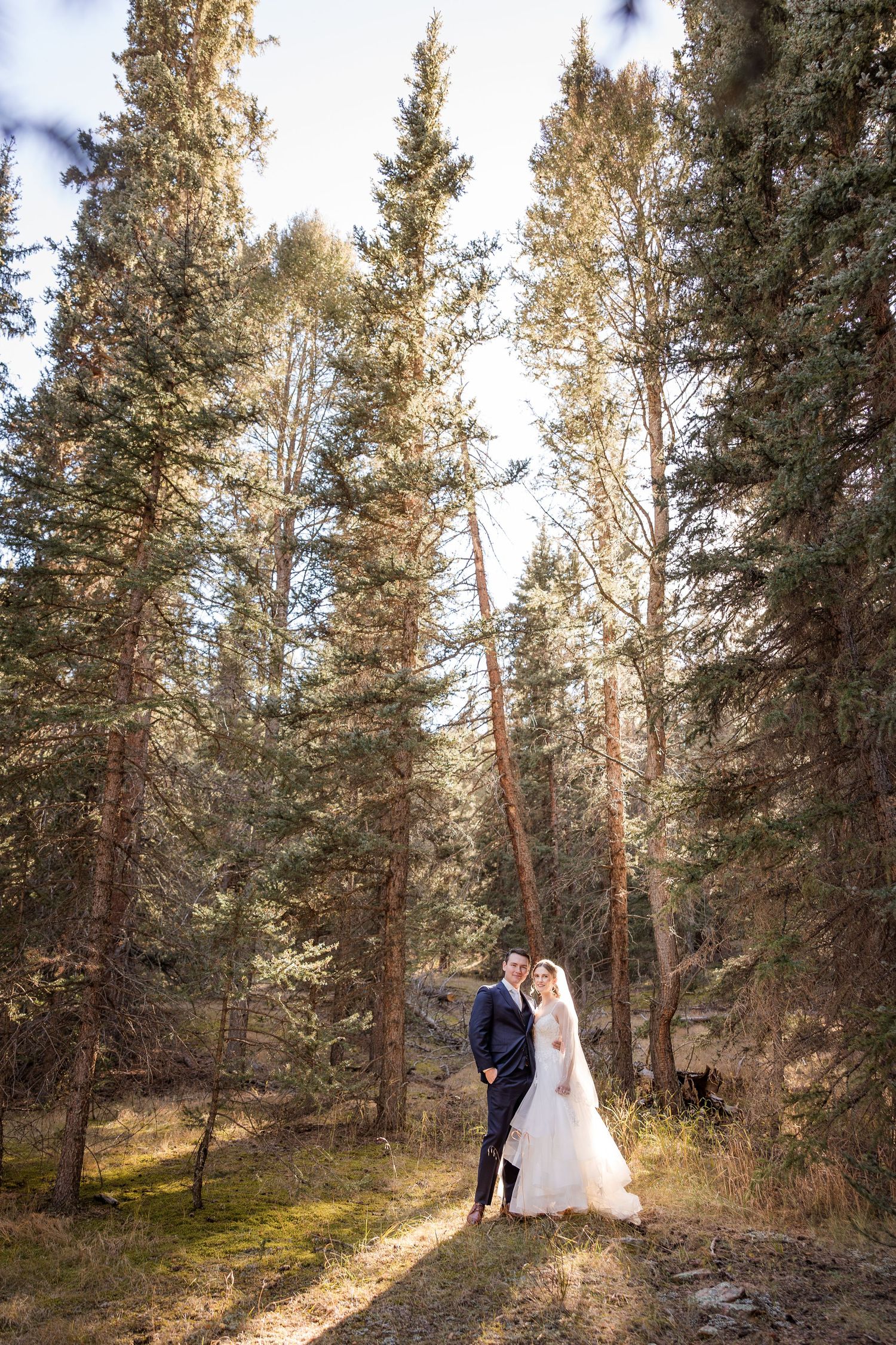 A couple in wedding attire dances together in a sunlit forest setting, creating a romantic outdoor scene.