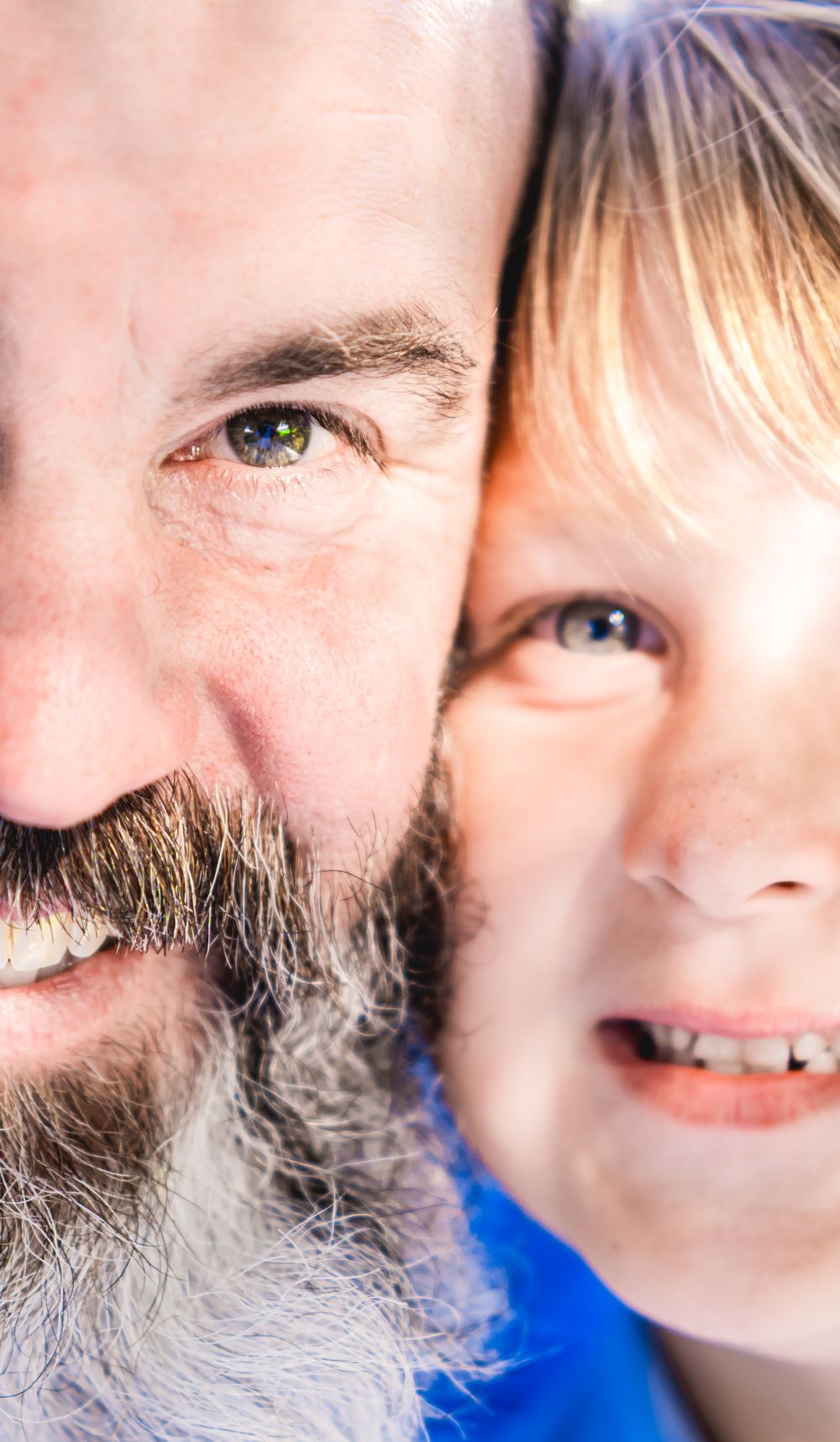 Close-up portrait of a smiling bearded father and a young blonde son cheek to cheek outdoors. Family Photographer.