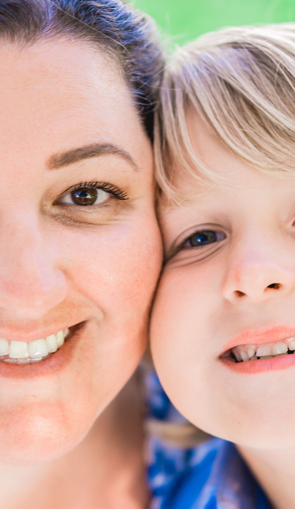 Close-up portrait of a smiling mother and young blonde child cheek to cheek outdoors. Family Photographer.
