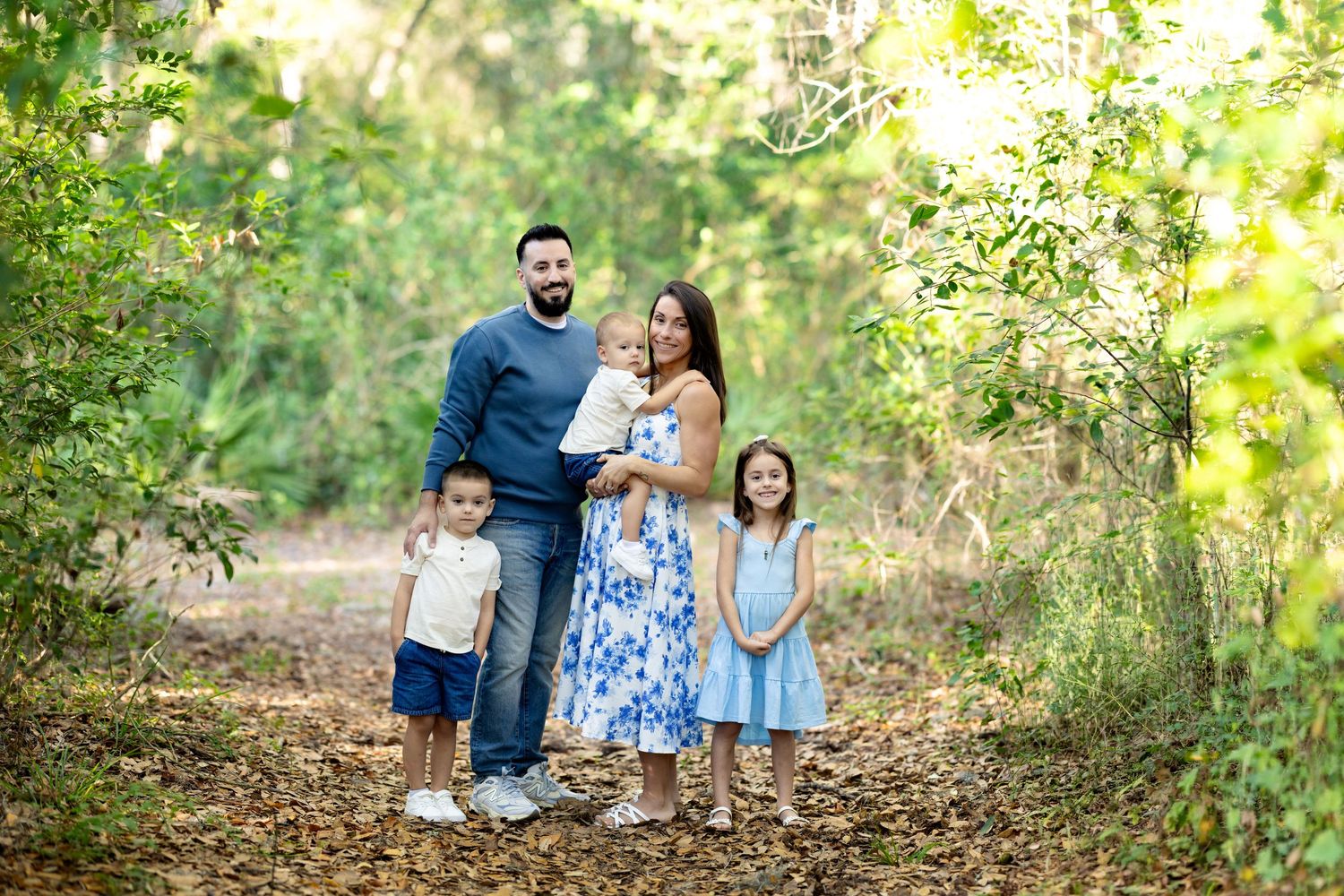 Family of five posing on a leafy trail surrounded by lush green trees during an outdoor portrait session.