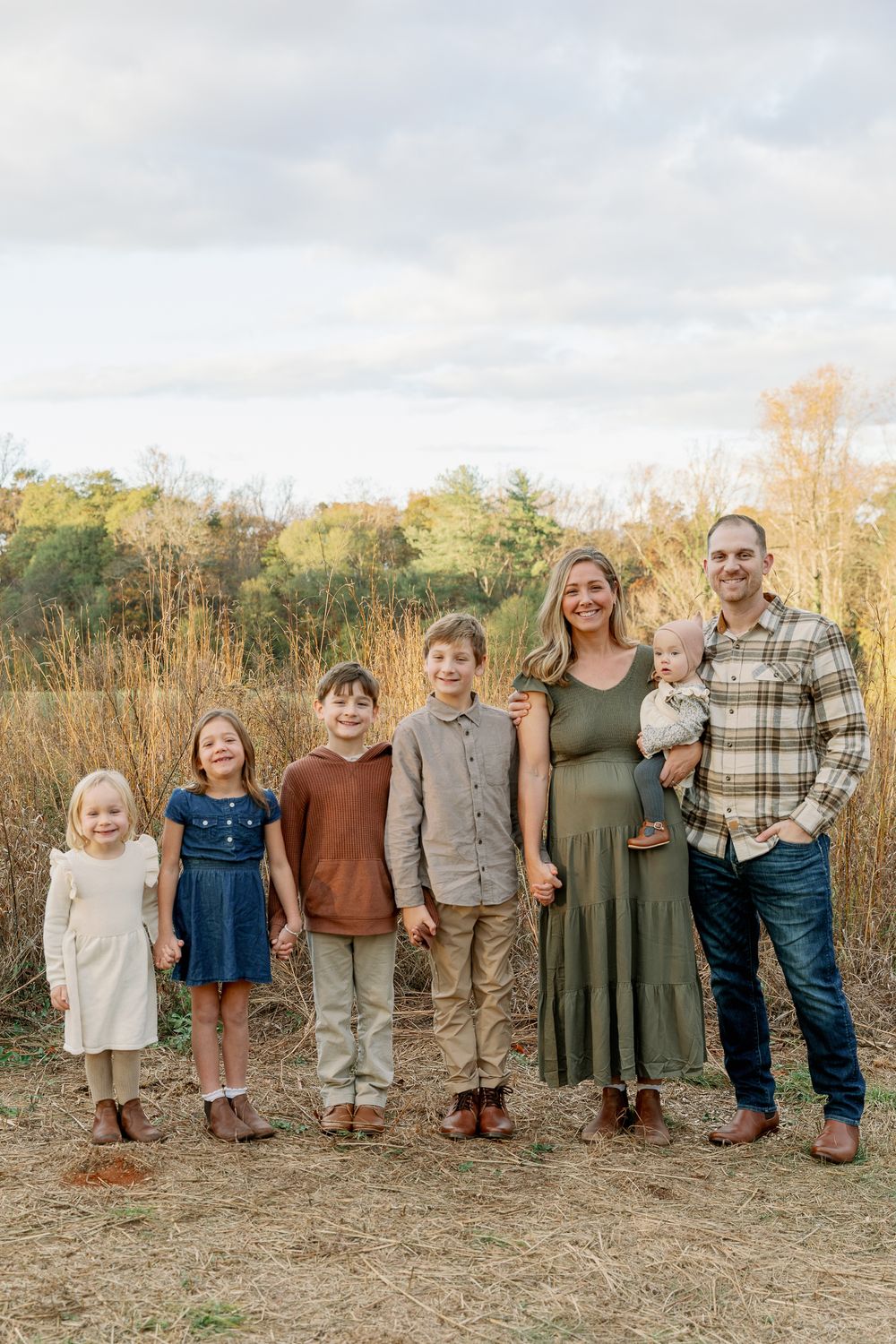Family of seven standing in a golden field during autumn, dressed in coordinated earth-tone outfits for a portrait.