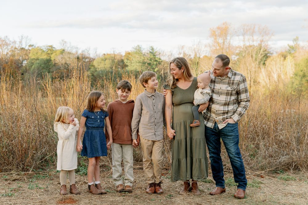 Family of six posing outdoors in autumn field, parents with four children in warm fall tones.