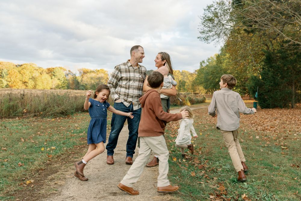 Family of six enjoying a walk on a scenic autumn path surrounded by colorful fall foliage.