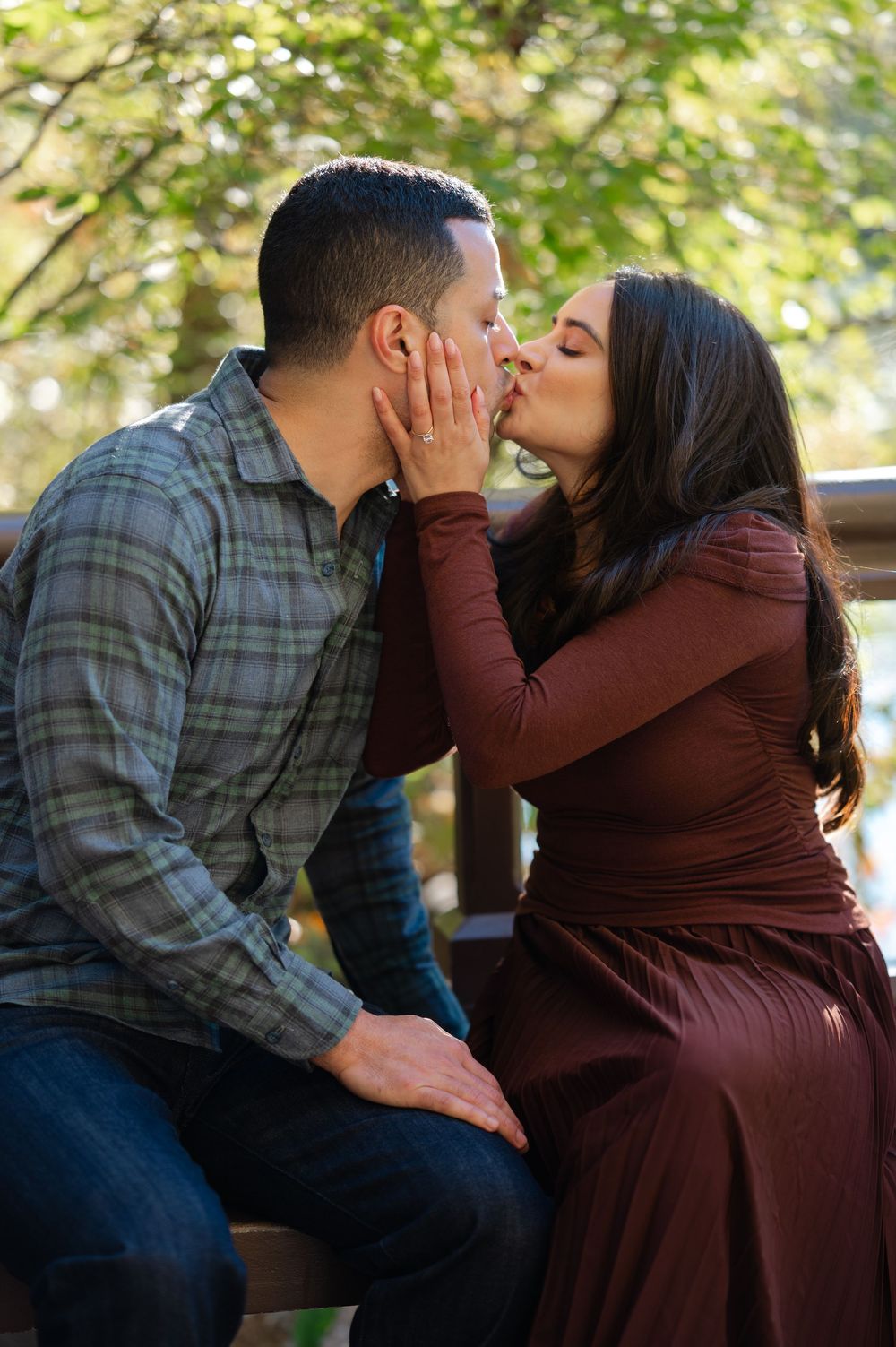 Couple sharing a romantic kiss outdoors, woman in burgundy dress and man in plaid shirt.