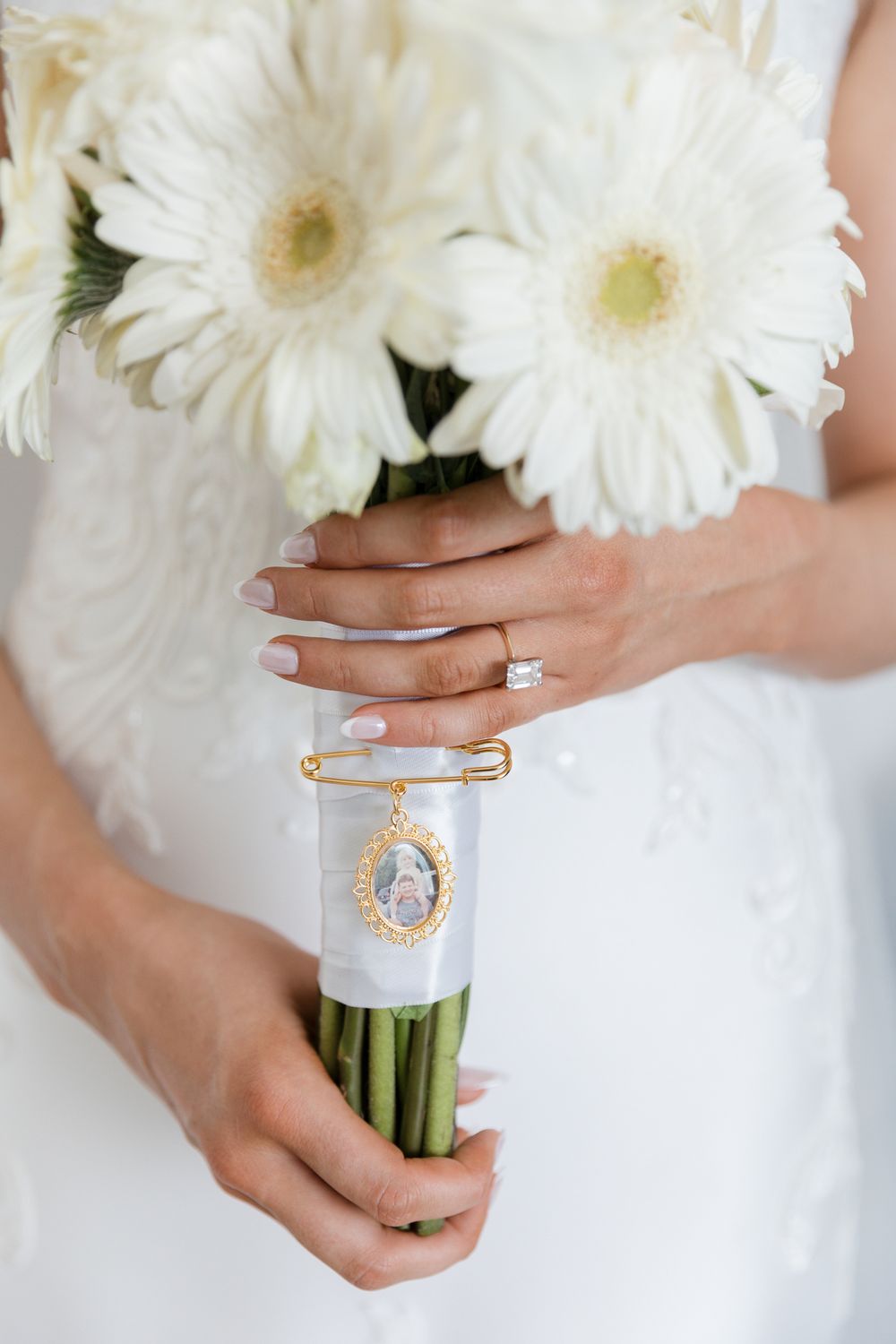 Bride holding white gerbera daisy bouquet with gold memorial photo charm pinned with safety pin.