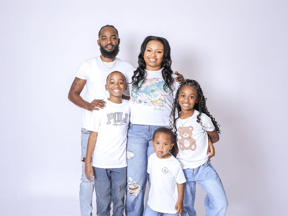 A joyful family of five poses together in white shirts and jeans against a white studio background.