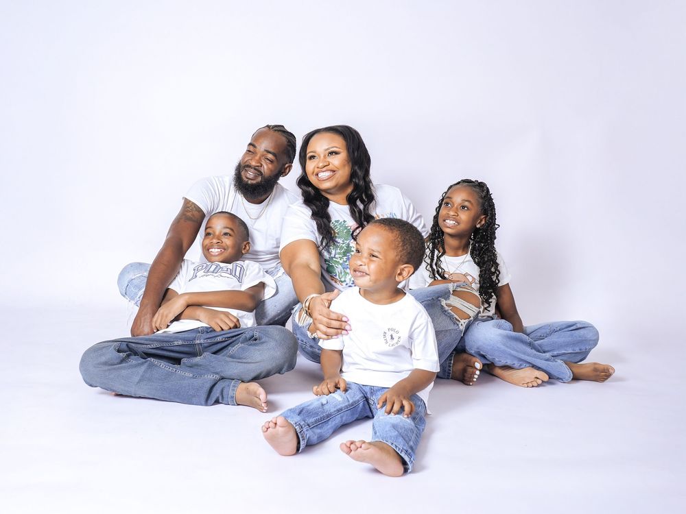 Happy Black family of five posing together in white outfits and jeans against a white studio background.
