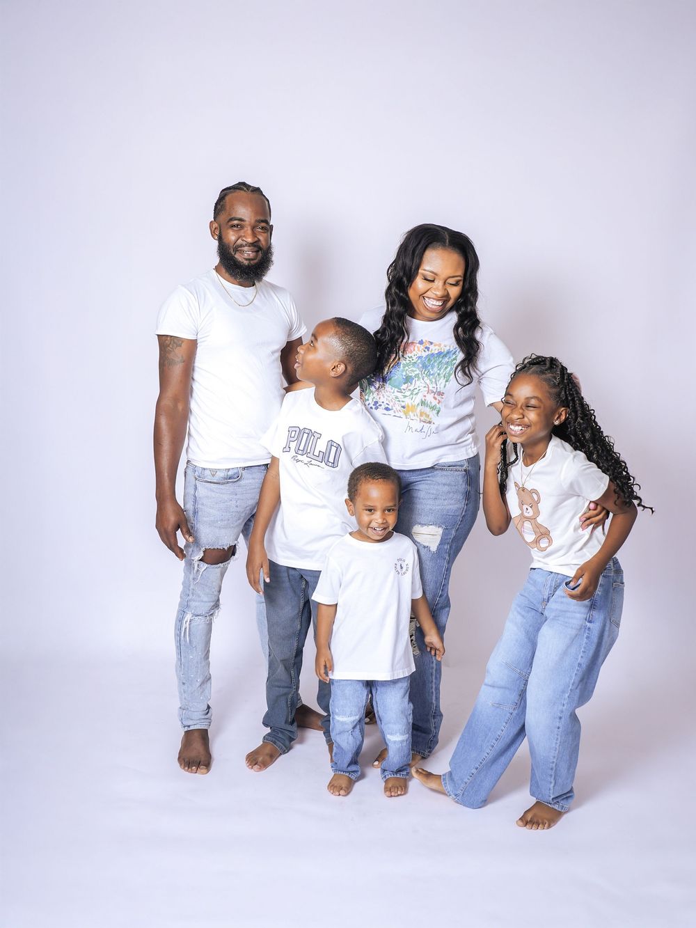 A joyful family of five in matching white tees and jeans poses together in a bright studio photo.