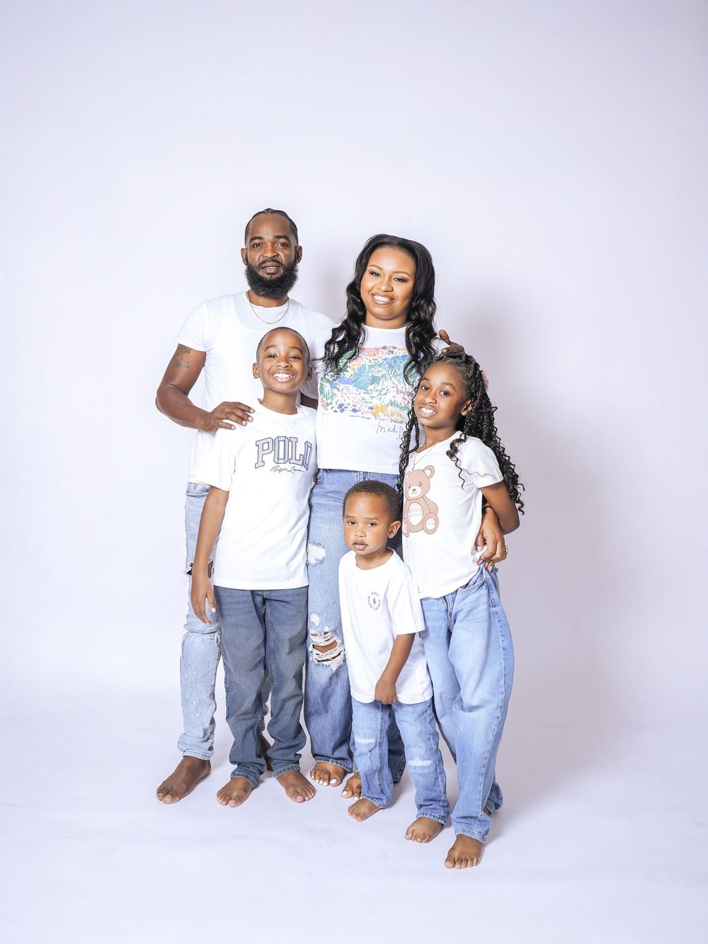 Family of five posing together in matching white shirts and jeans for a professional studio portrait photo.