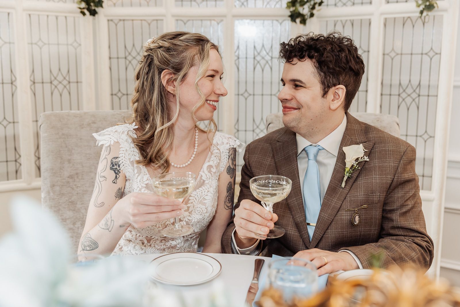 A bride and groom share a toast with champagne glasses, smiling at each other during their wedding reception.