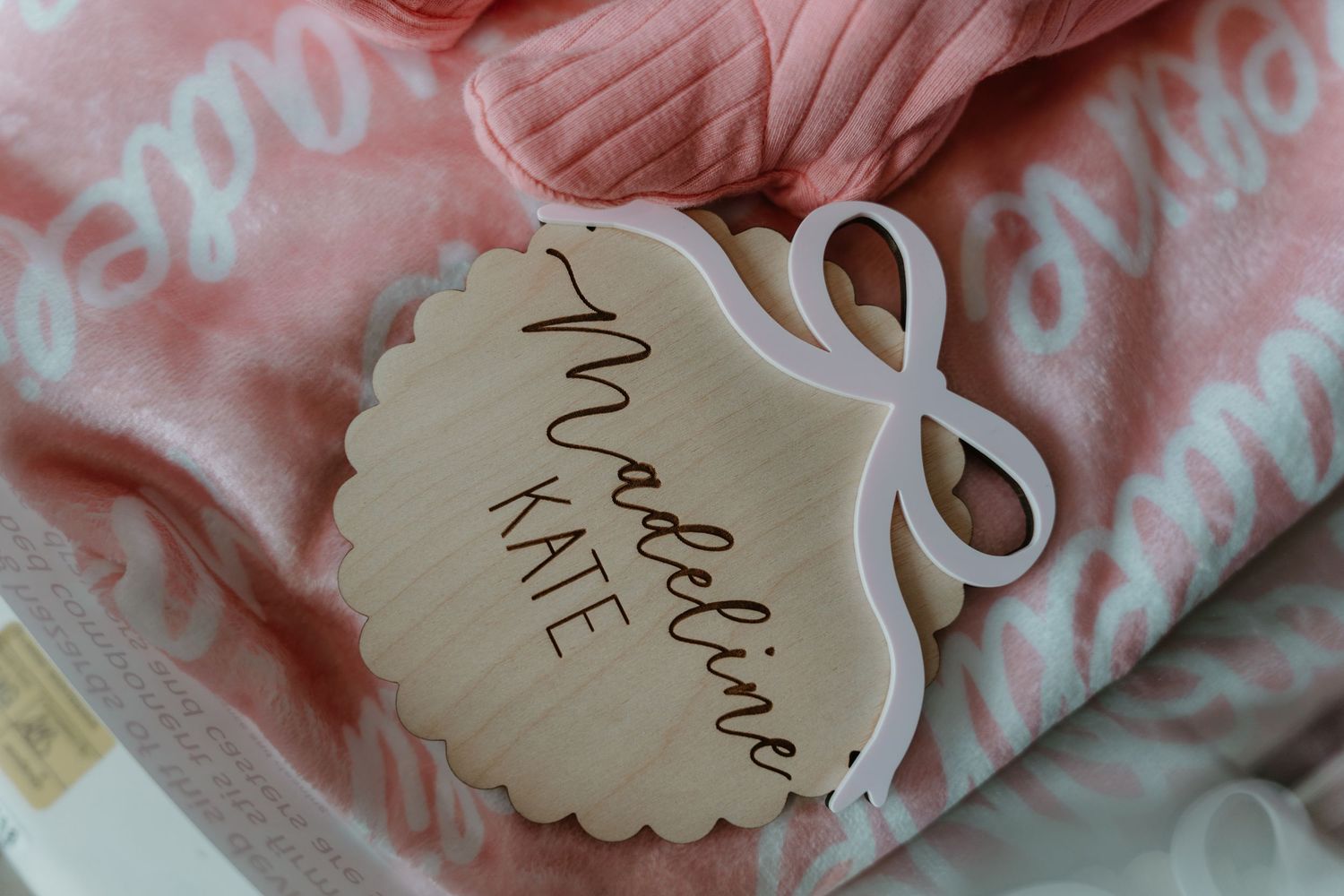 Personalized wooden baby name tag reading Madeline Kate on pink monogrammed baby blanket.