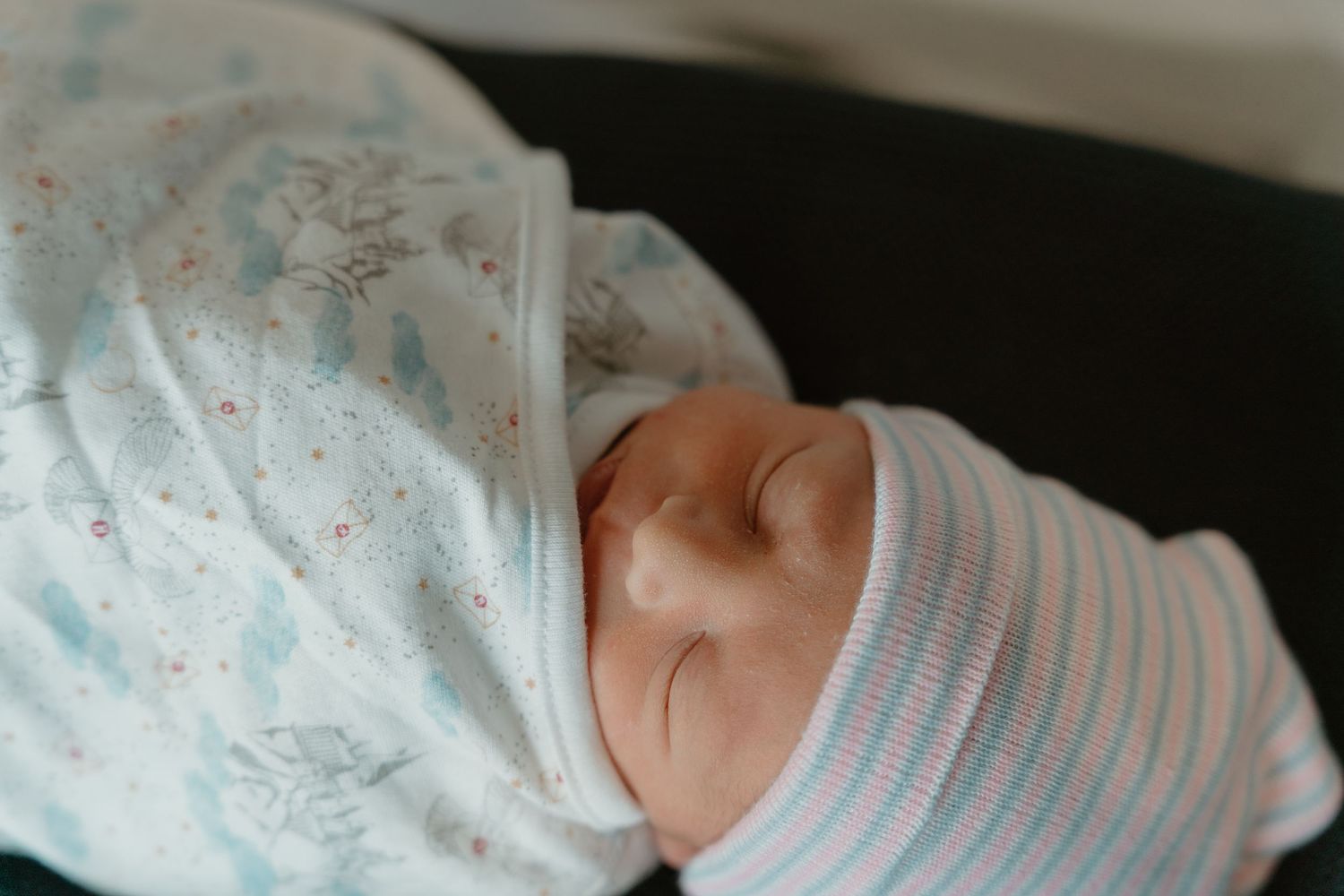 Swaddled newborn baby sleeping in a hospital blanket with a striped newborn hat.