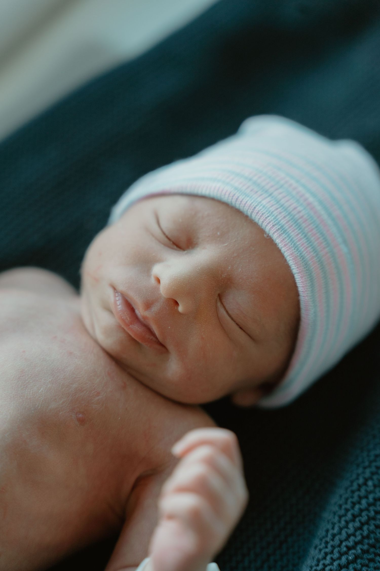 Peaceful newborn baby sleeping in a white and pink striped hospital hat on a teal blanket.