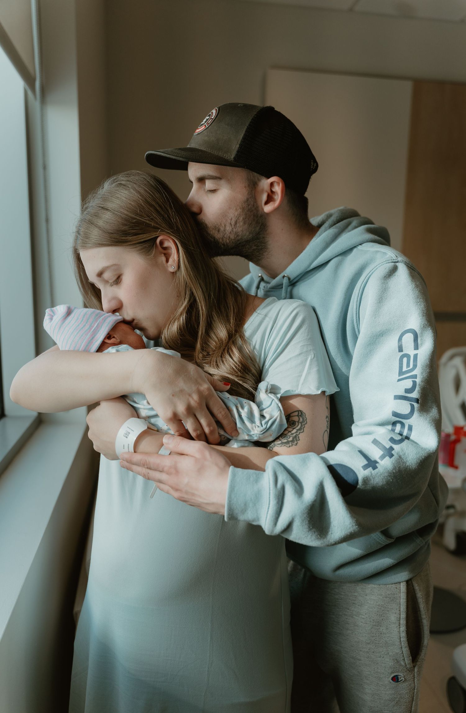 New parents sharing a tender moment holding their newborn baby by a hospital window.
