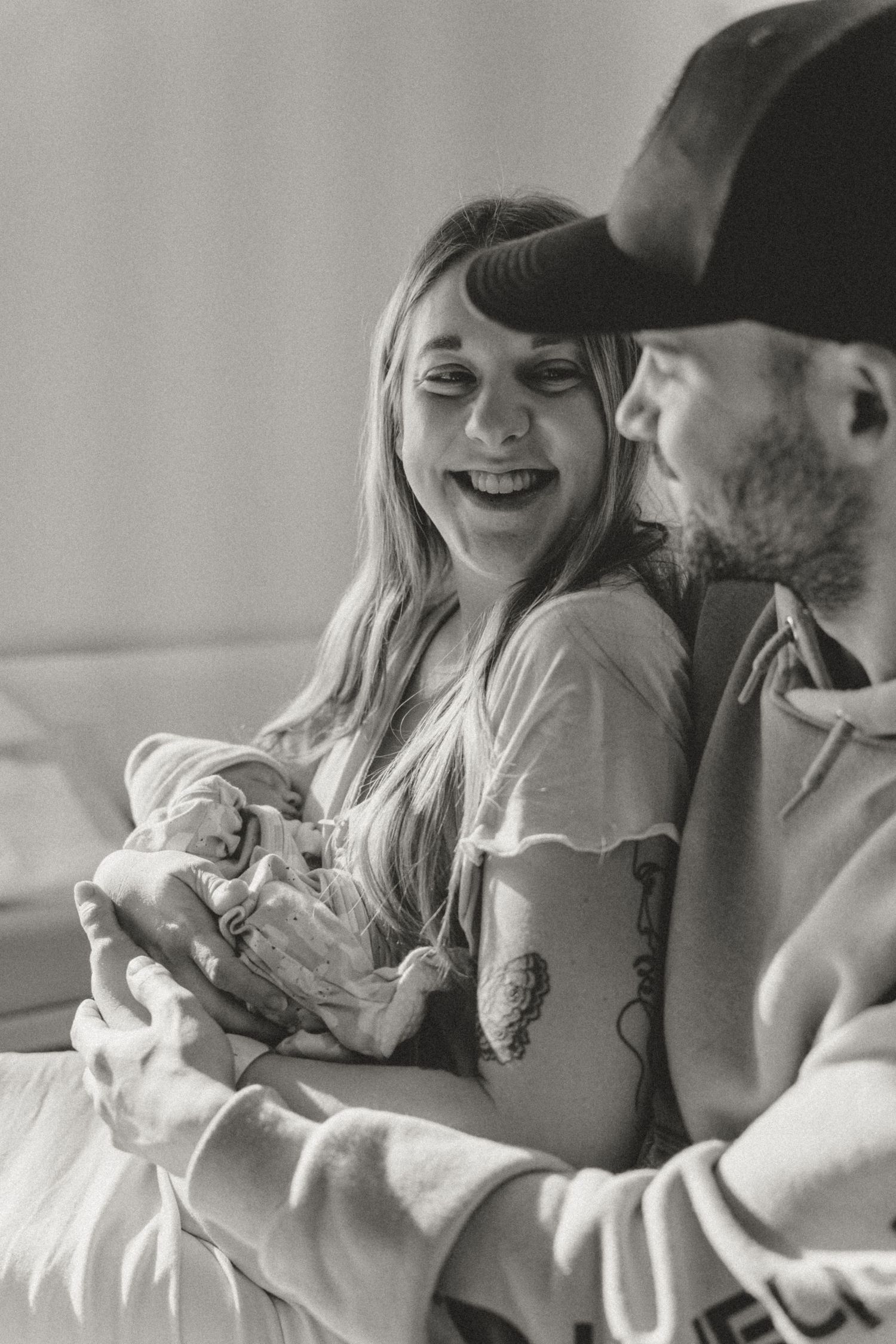 Happy mother laughing while holding newborn baby with father beside her in black and white.