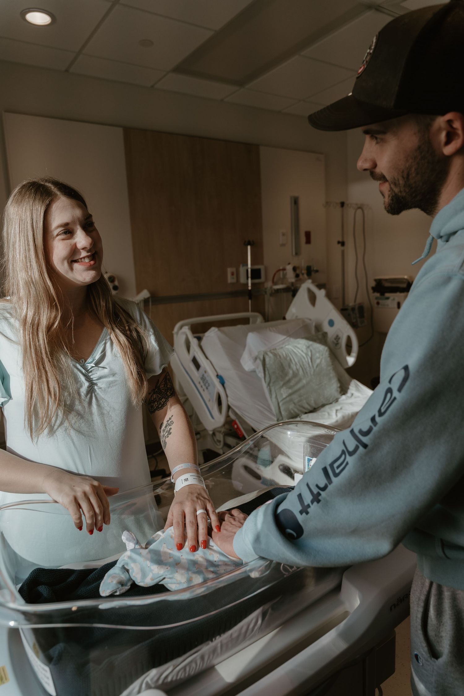 Smiling new mother and father admiring their newborn baby in a hospital room bassinet.