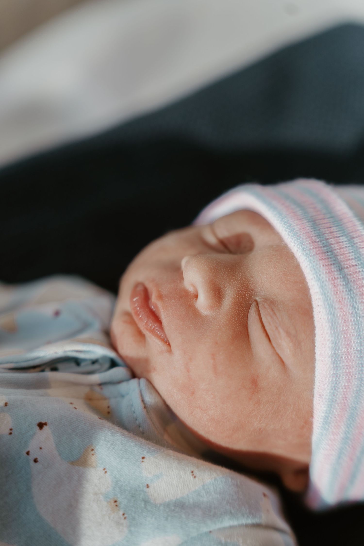 Close-up portrait of a sleeping newborn baby wearing a pink and blue striped hospital hat.