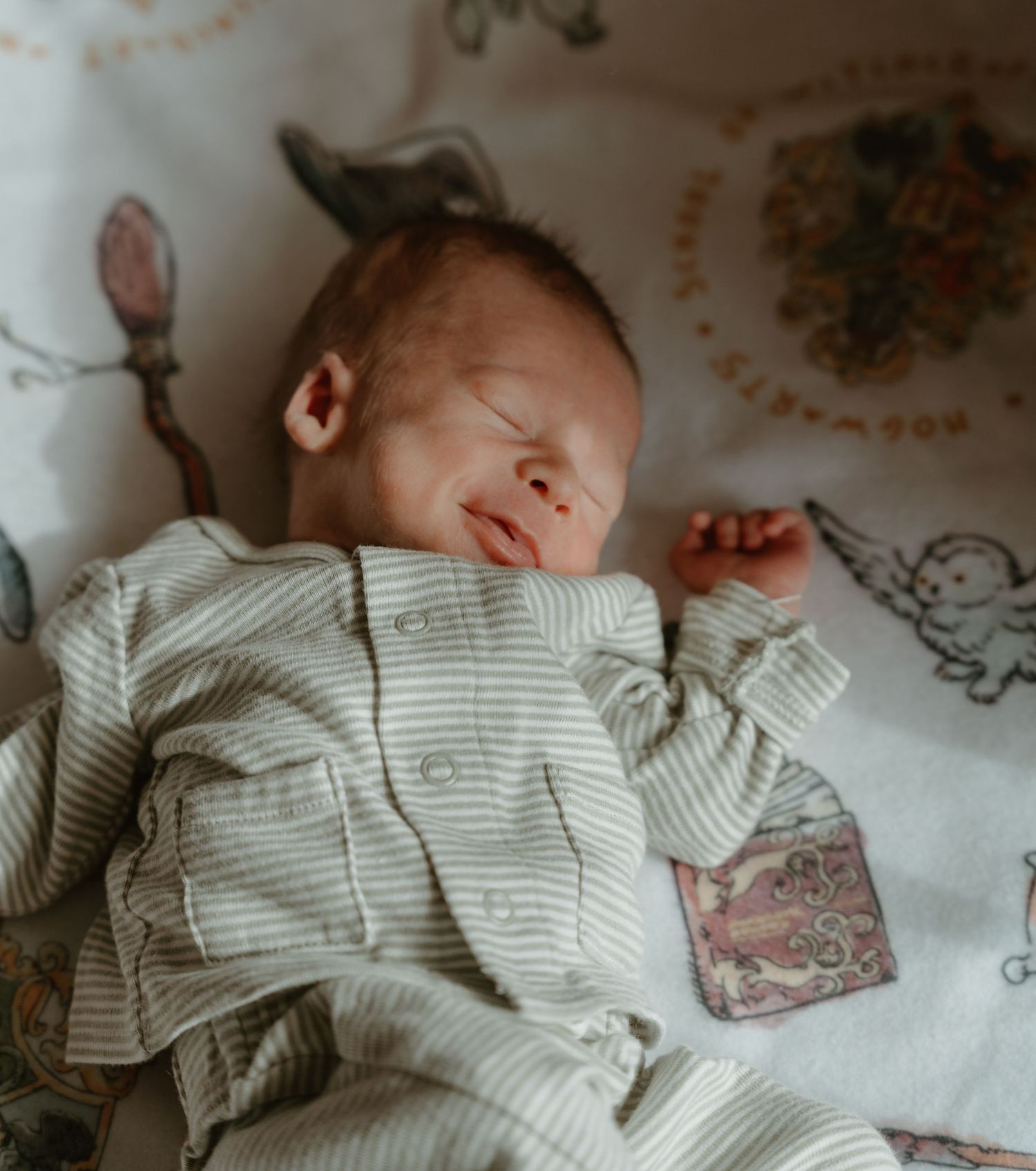 Peaceful sleeping newborn baby in sage green striped onesie on woodland animal nursery blanket.