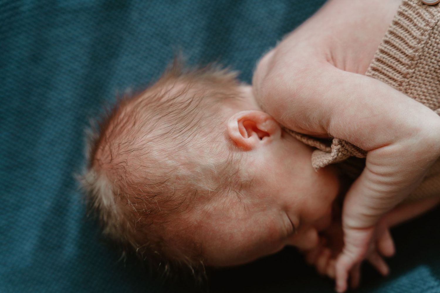 Close-up of a newborn baby breastfeeding, with tiny fingers visible against mothers hand.