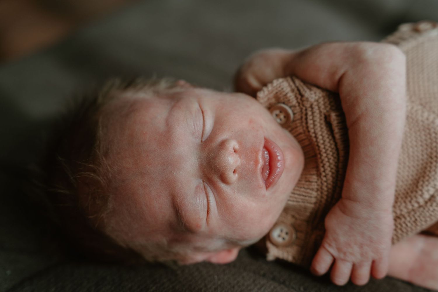Close-up of a sleeping newborn baby in a beige knit outfit with tiny hands visible.