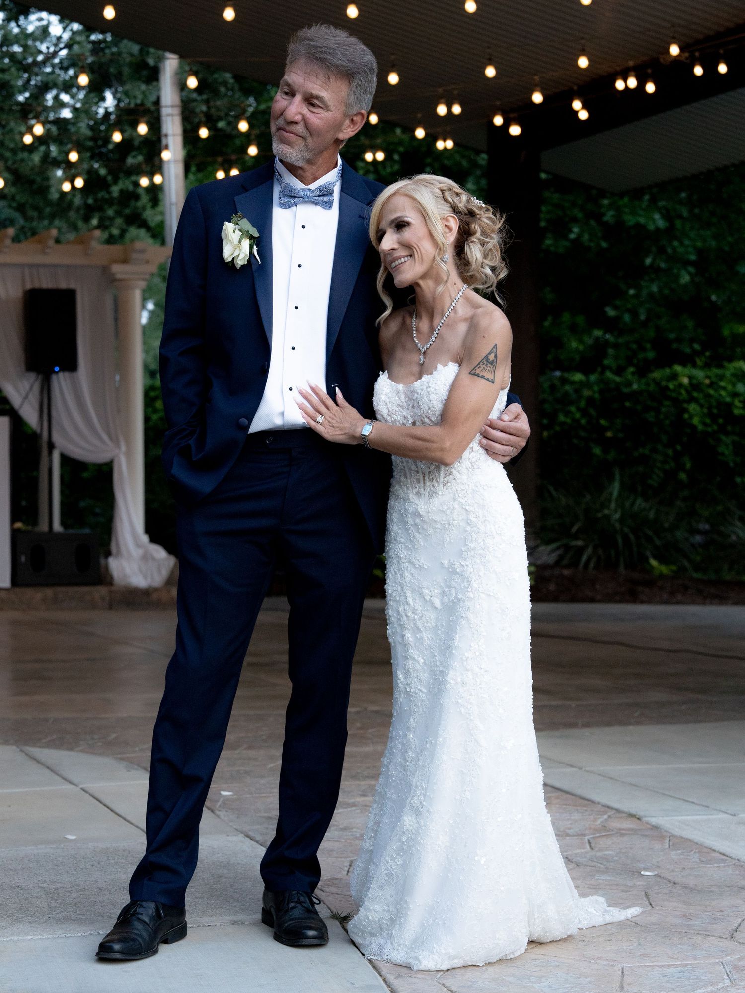 Bride and groom posing elegantly at outdoor wedding reception with string lights overhead.