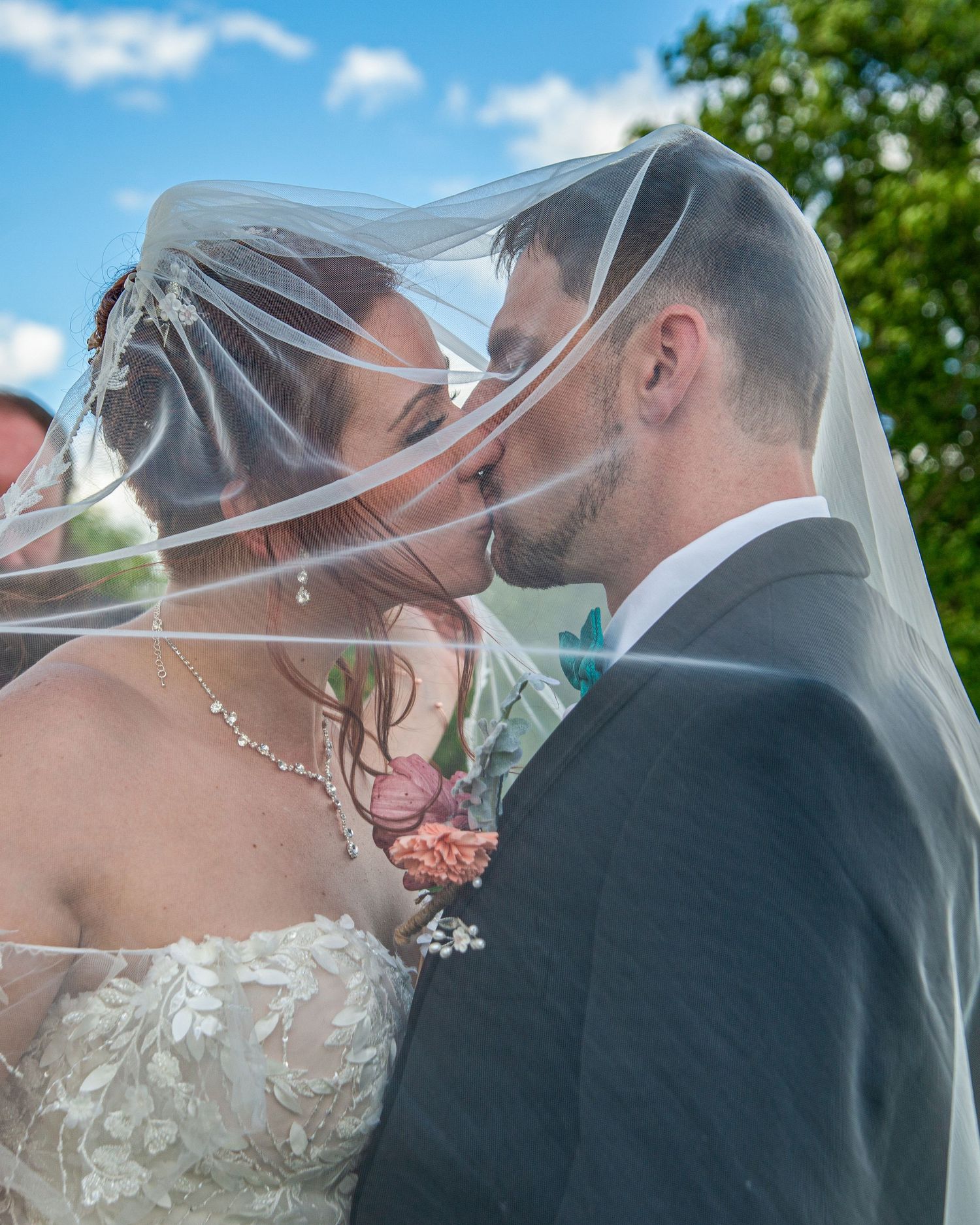 A bride and groom hold Mr and Mrs signs while sharing a kiss outdoors with scenic green hills in the background.