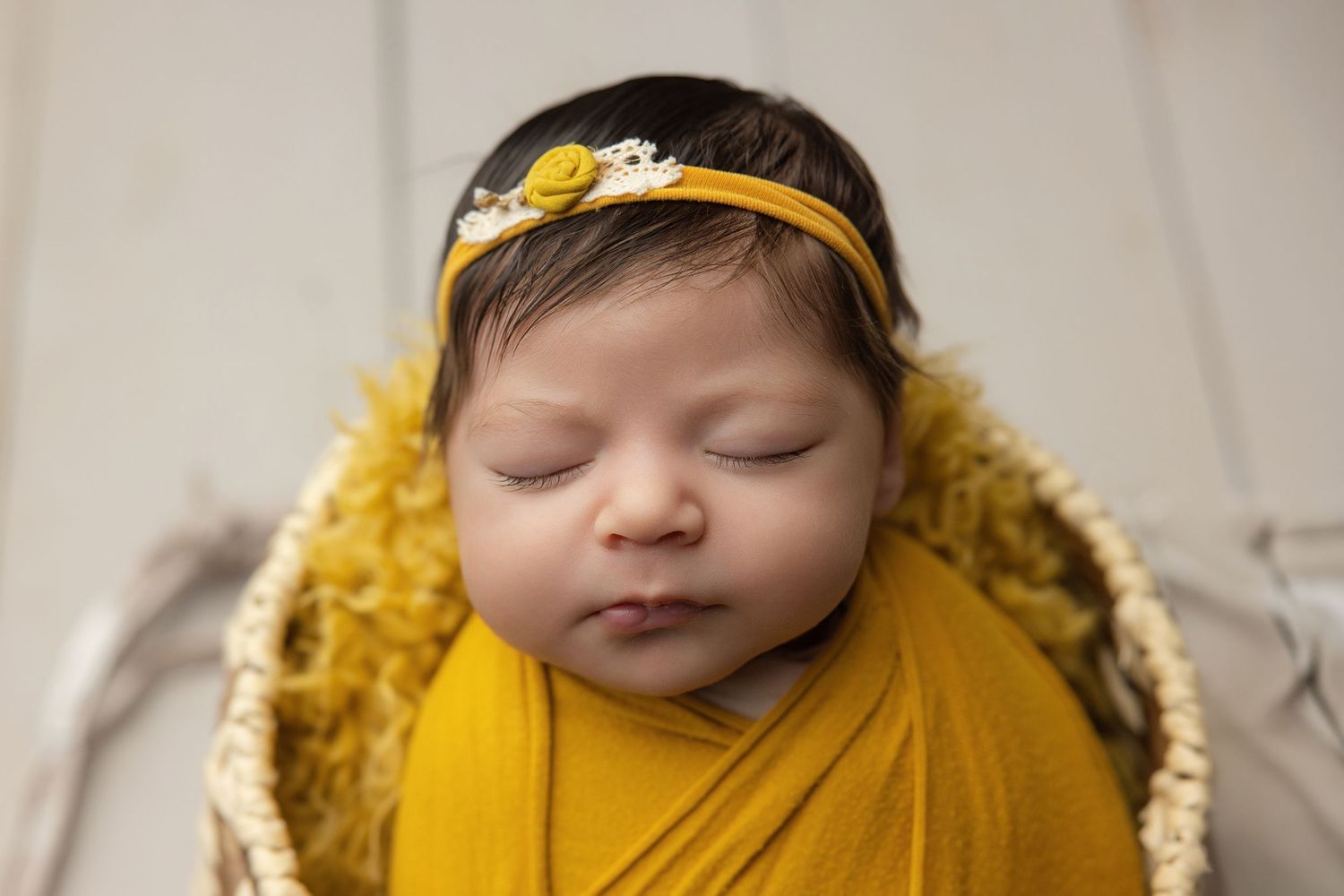 Sleeping newborn baby wrapped in teal swaddle inside a small bucket with a green pillow.
