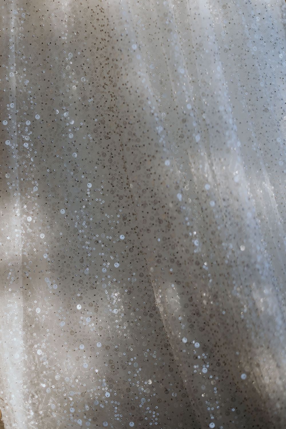 Macro detail shot of a sparkling wedding dress fabric with sequins and bokeh light reflections.