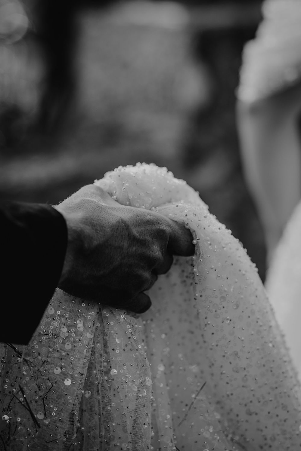 Close-up black and white photo of groom holding bride's embellished wedding veil.