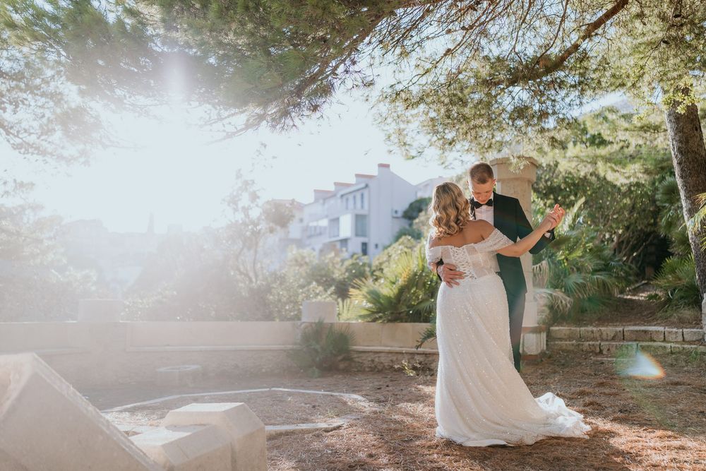 Bride and groom share romantic embrace in sunlit outdoor garden wedding setting.
