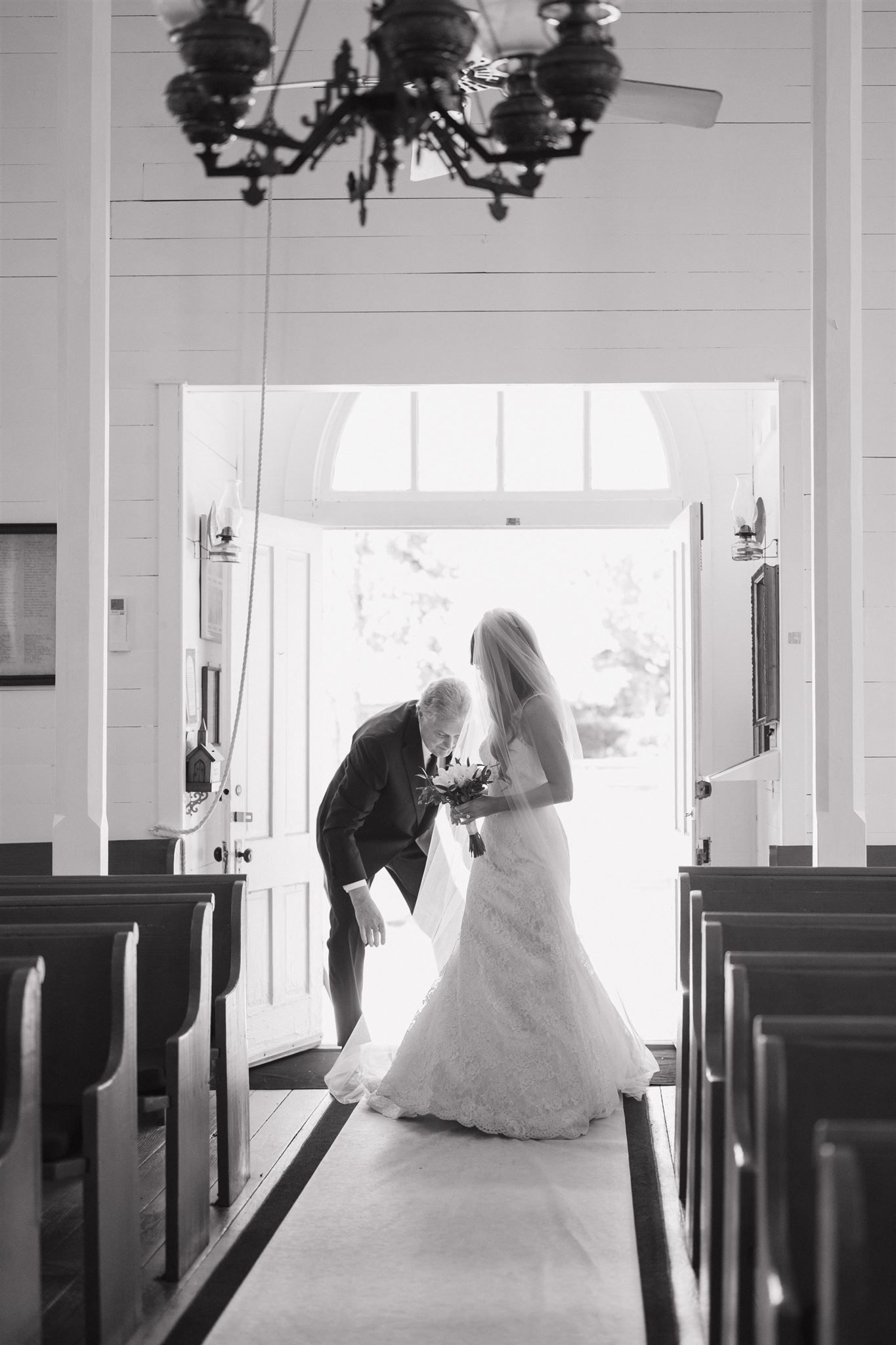 Black and white photo of a bride and her father sharing a tender moment at Tomball church doors on her wedding day.